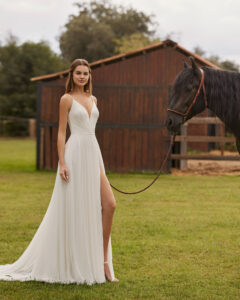 Robe de Mariée Niler collection Alma Novia 2026. Robe légère plis mousseline fente avec cape. Essayer boutique mariage showroom Paris