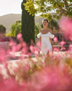 Robe de Mariée Sabila Adriana Alier 2026. Robe bustier stylée grosses fleurs blanches épaules tombantes. Essayer boutique mariage Paris