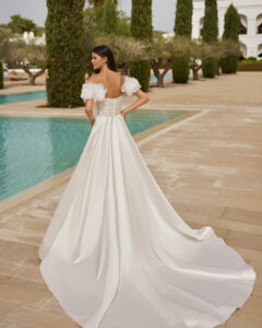 Robe de Mariée Suiza Adriana Alier 2026. Robe bustier volume stylée grosses fleurs blanches épaules tombantes. RDV boutique mariage Paris