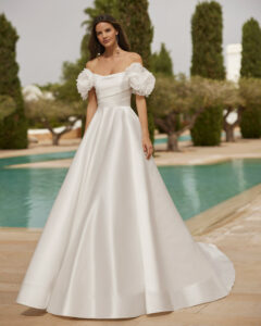 Robe de Mariée Suiza Adriana Alier 2026. Robe bustier volume stylée grosses fleurs blanches épaules tombantes. RDV boutique mariage Paris
