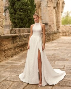 Robe de Mariée Prado Adriana Alier 2027 boutique mariage paris. robe col américain évasée fendue matière brocart. Fente ajustable